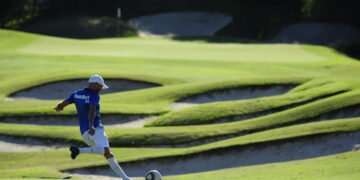 Ballon de soccer près d'un trou sur un parcours de footgolf, illustrant la fusion du football et du golf.